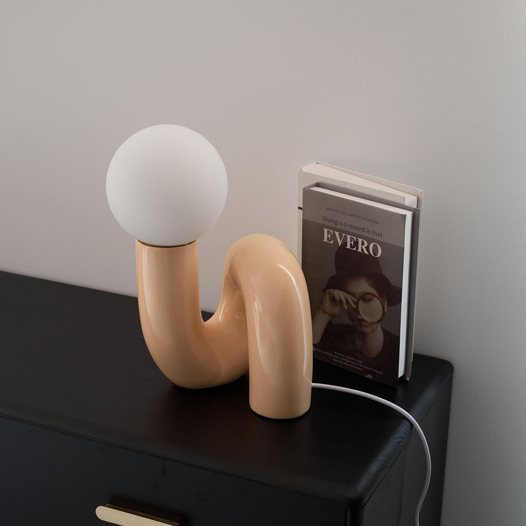 Peach Clérachic table lamp on a black cabinet with a book beside it, its white cord hanging down the side.