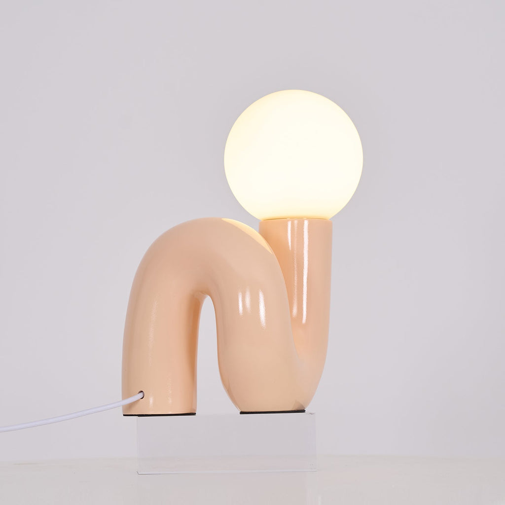 Lit peach Clérachic table lamp on a clear block, its glossy tube base curving below a warm globe.