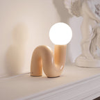 Lit peach Clérachic table lamp on a white ledge, its warm globe beside a cherub statue.
