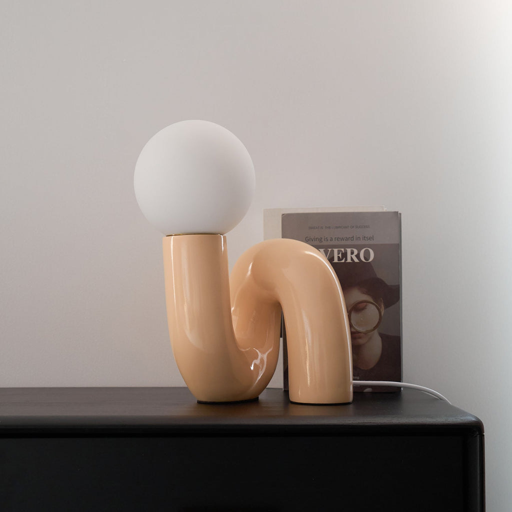 Peach Clérachic table lamp with an unlit globe on a black cabinet, a book standing behind the curved base.