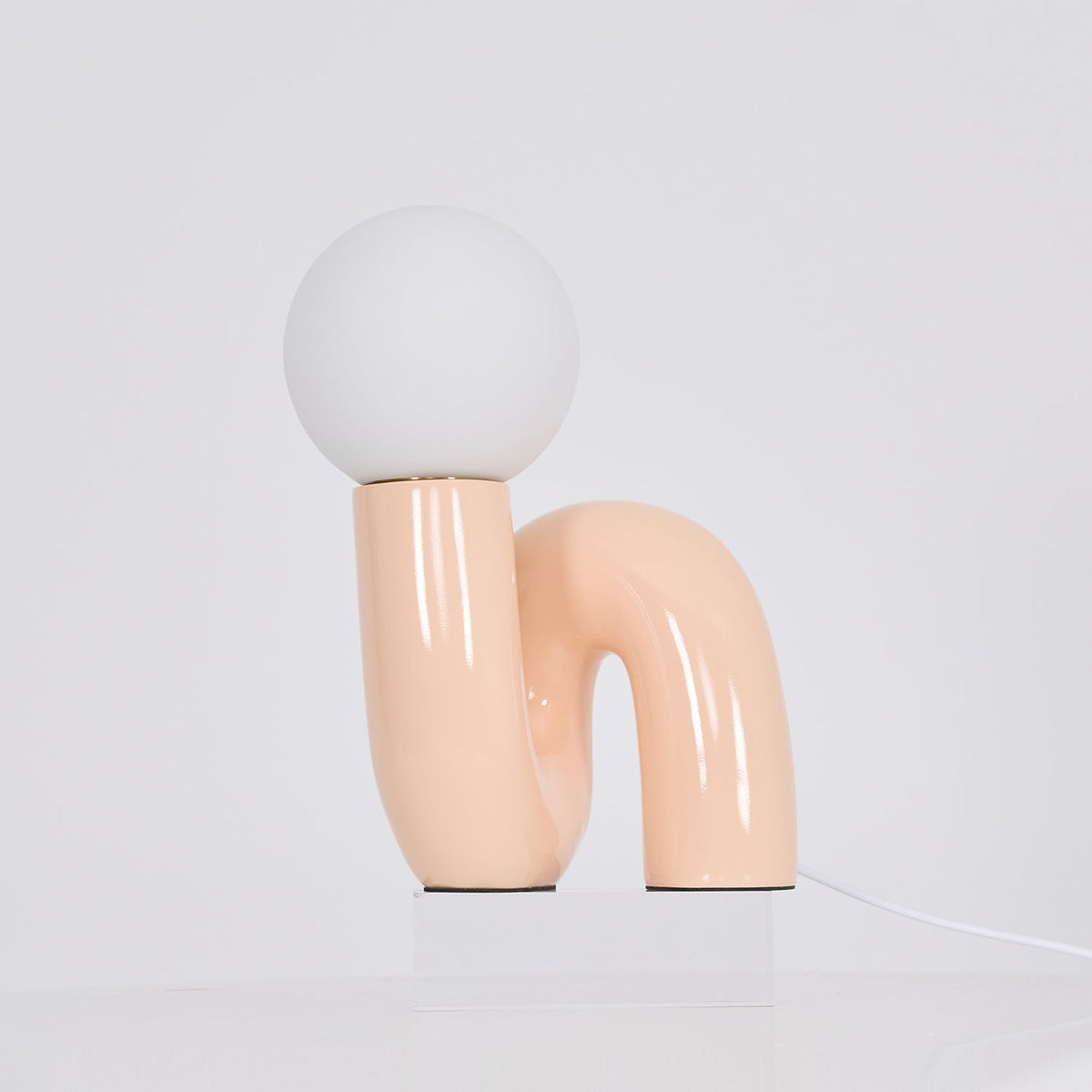 Peach Clérachic table lamp on a clear block against a pale backdrop, its globe unlit and cord to the right.