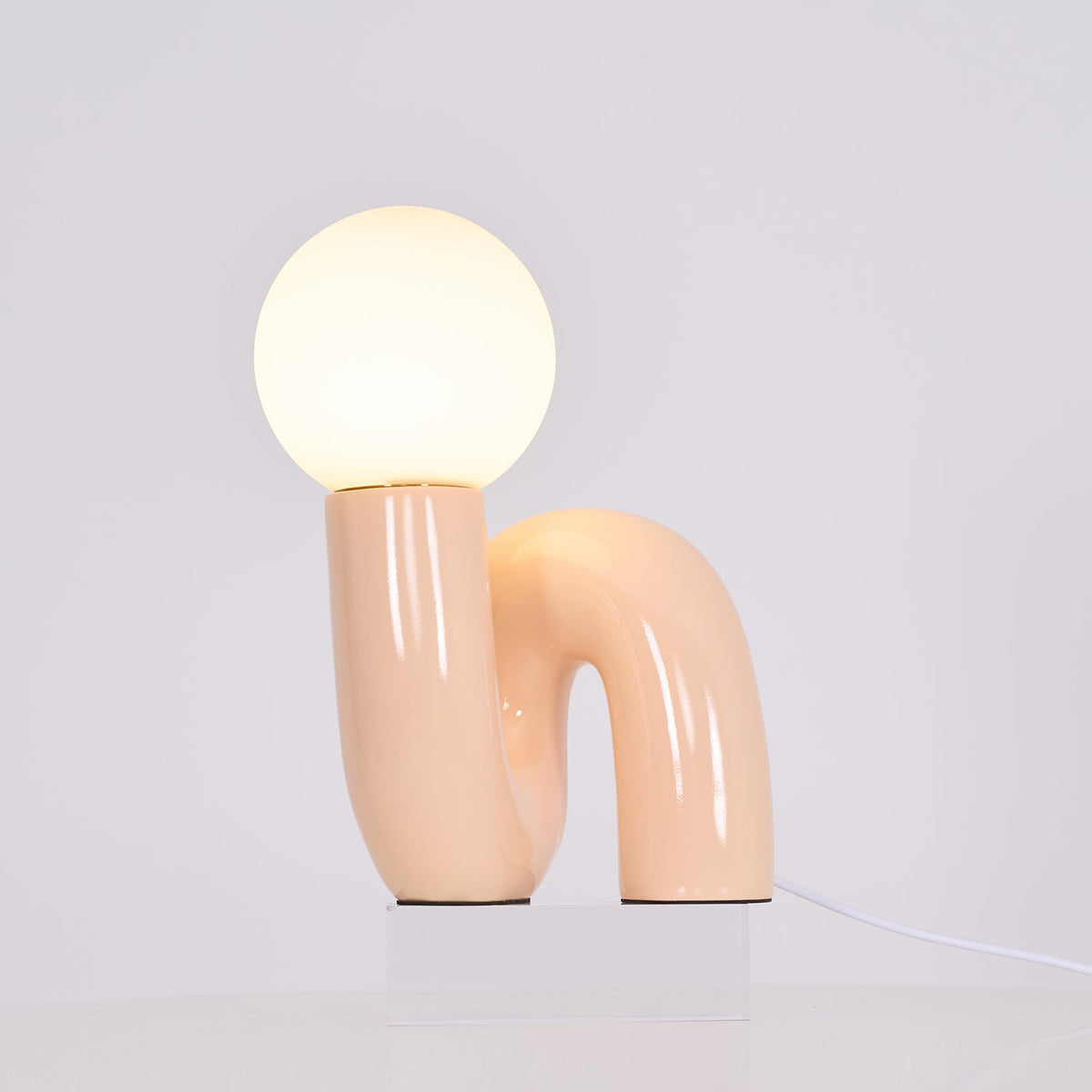 Lit peach Clérachic table lamp on a clear block, a warm glow spreading from the globe over the base.
