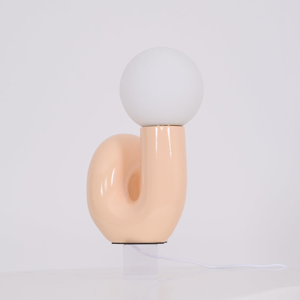 Peach Clérachic table lamp seen from the side on a clear block, the looped base curving to the left.