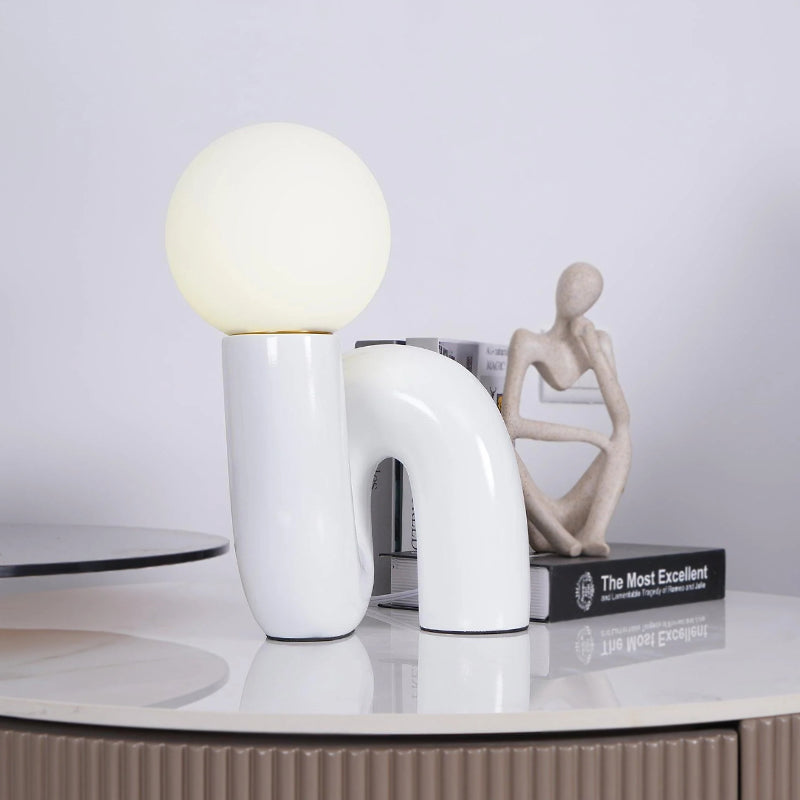 White Clérachic table lamp on a marble top, a seated stone figure and a stack of books at its side.