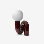 Dark red Clérachic table lamp on a white backdrop, a glossy tube base coiled under a frosted globe.