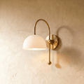 Clérachic wall lamp in brass with a white dome shade on an arched arm ending in a ball finial.