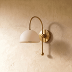 This brass Clérachic wall lamp is shown from another angle, its white dome shade glowing softly.