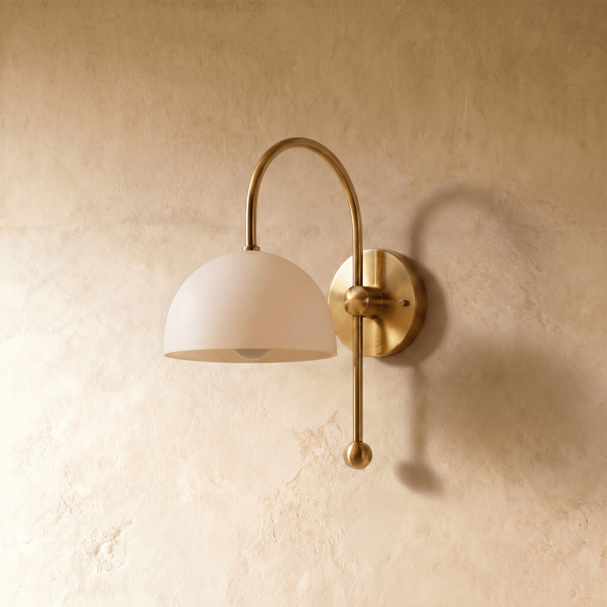 This brass Clérachic wall lamp is shown from another angle, its white dome shade glowing softly.