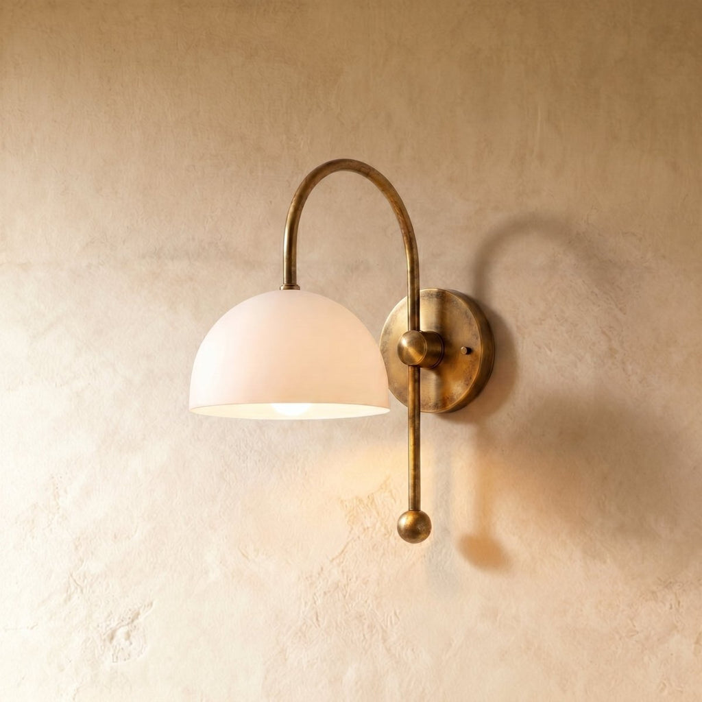 Clérachic wall lamp in vintage brass, its white dome shade curving from an arched arm and ball finial.