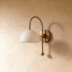 This vintage brass Clérachic wall lamp is shown from a different angle, the dome shade lit warmly.