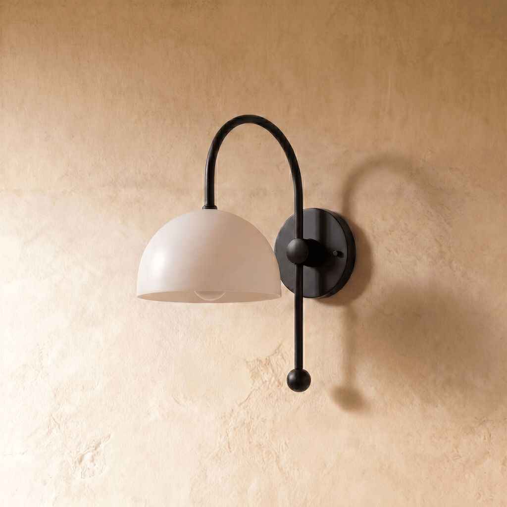 This black Clérachic wall lamp is shown from another angle, its white dome shade glowing softly.
