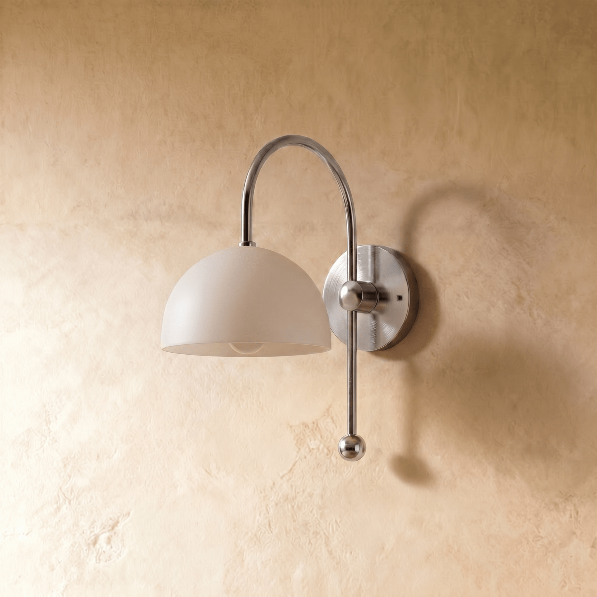 This chrome Clérachic wall lamp is shown from a different angle, the dome shade lit warmly.