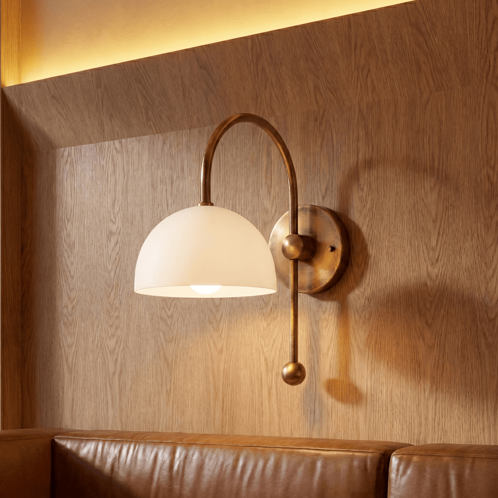 This vintage brass Clérachic wall lamp lights a wood-paneled wall above a tan leather sofa.