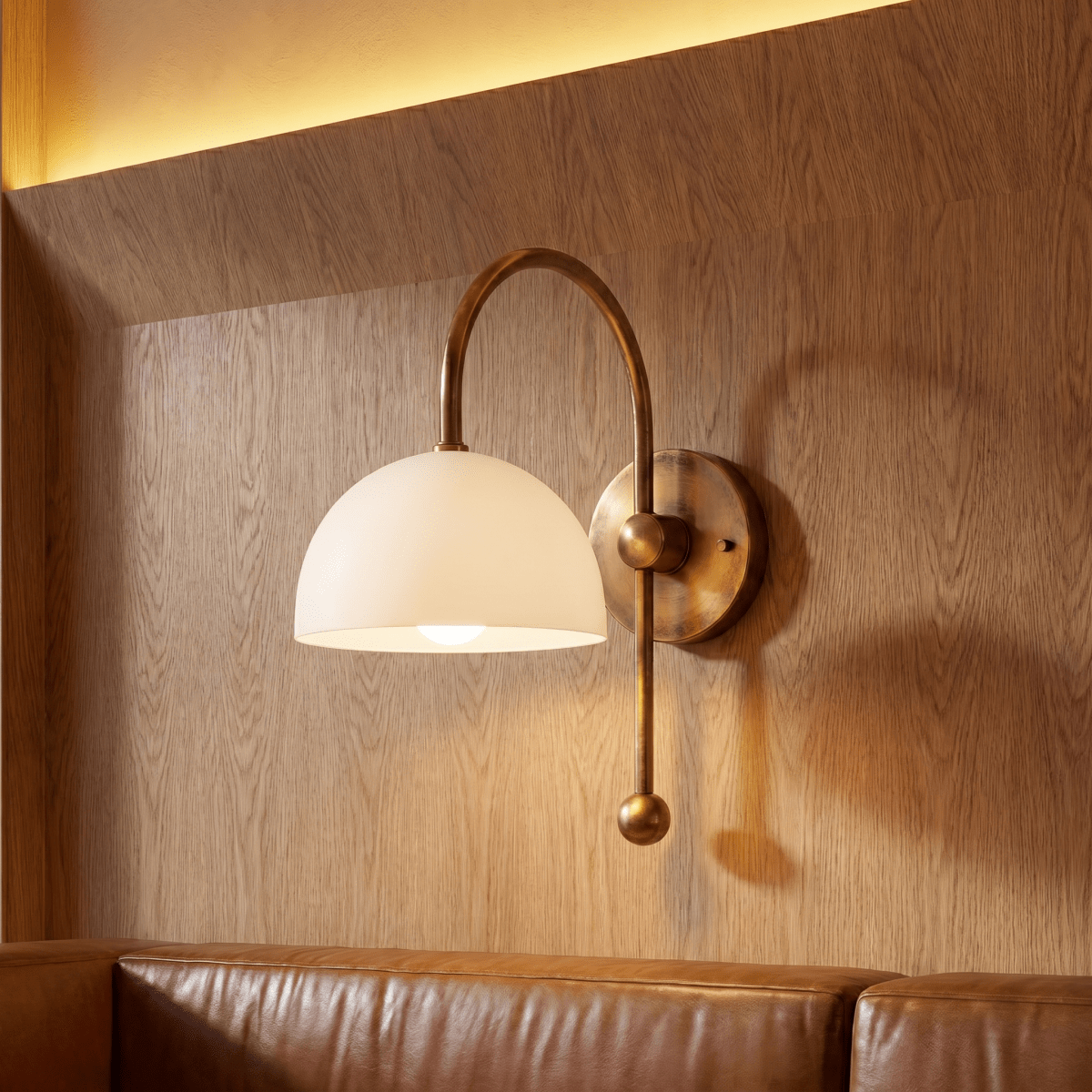 This vintage brass Clérachic wall lamp lights a wood-paneled wall above a tan leather sofa.