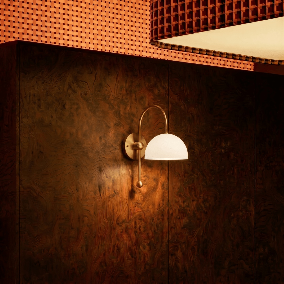 This brass Clérachic wall lamp with a glass globe lights a wood-panelled wall above a woven bench seat.
