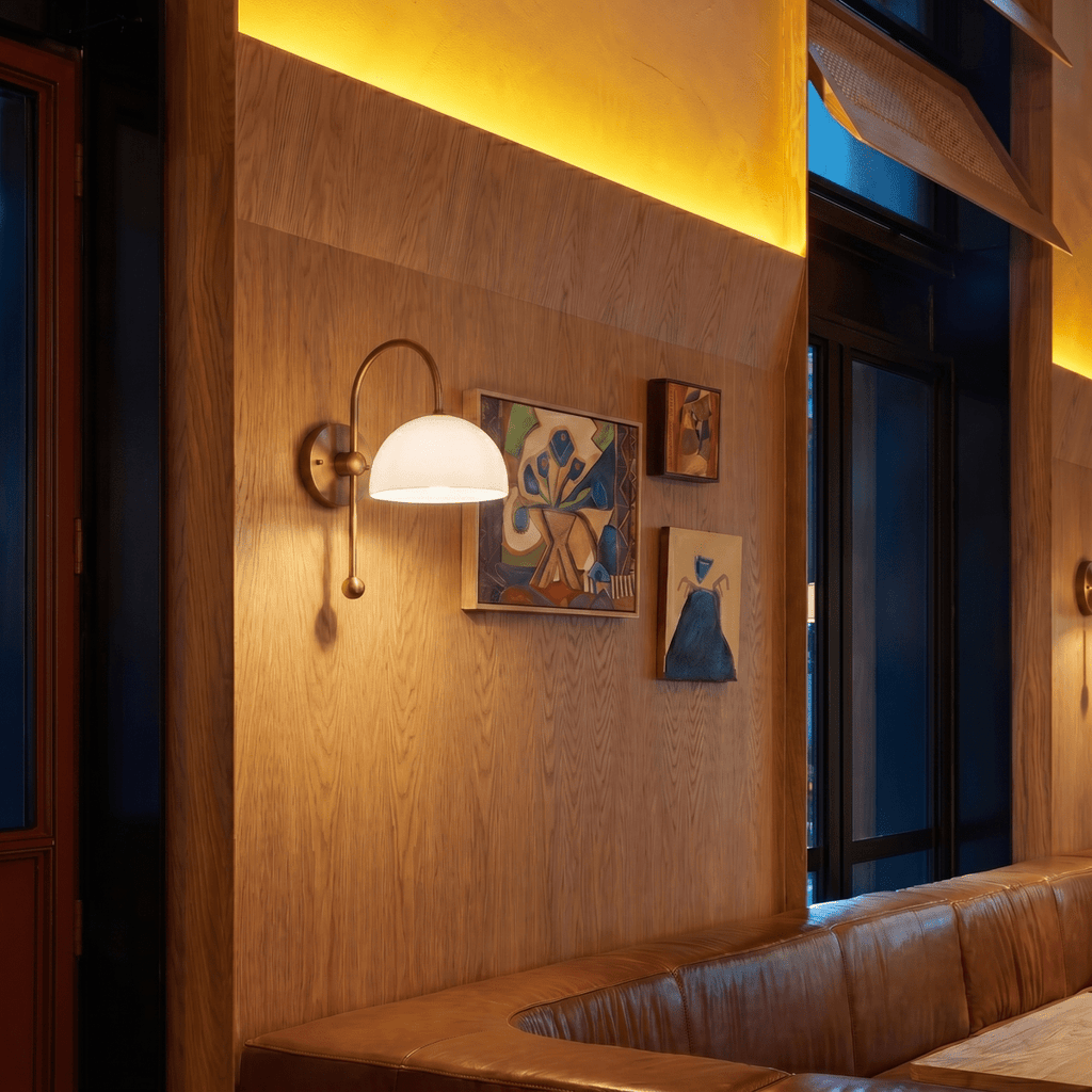 A vintage brass Clérachic wall lamp lights a restaurant booth beside a gallery of framed paintings.