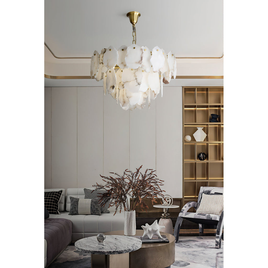 The Gloire alabaster chandelier from Clérachic lighting a pale living room above a tufted sofa and a round marble coffee table.