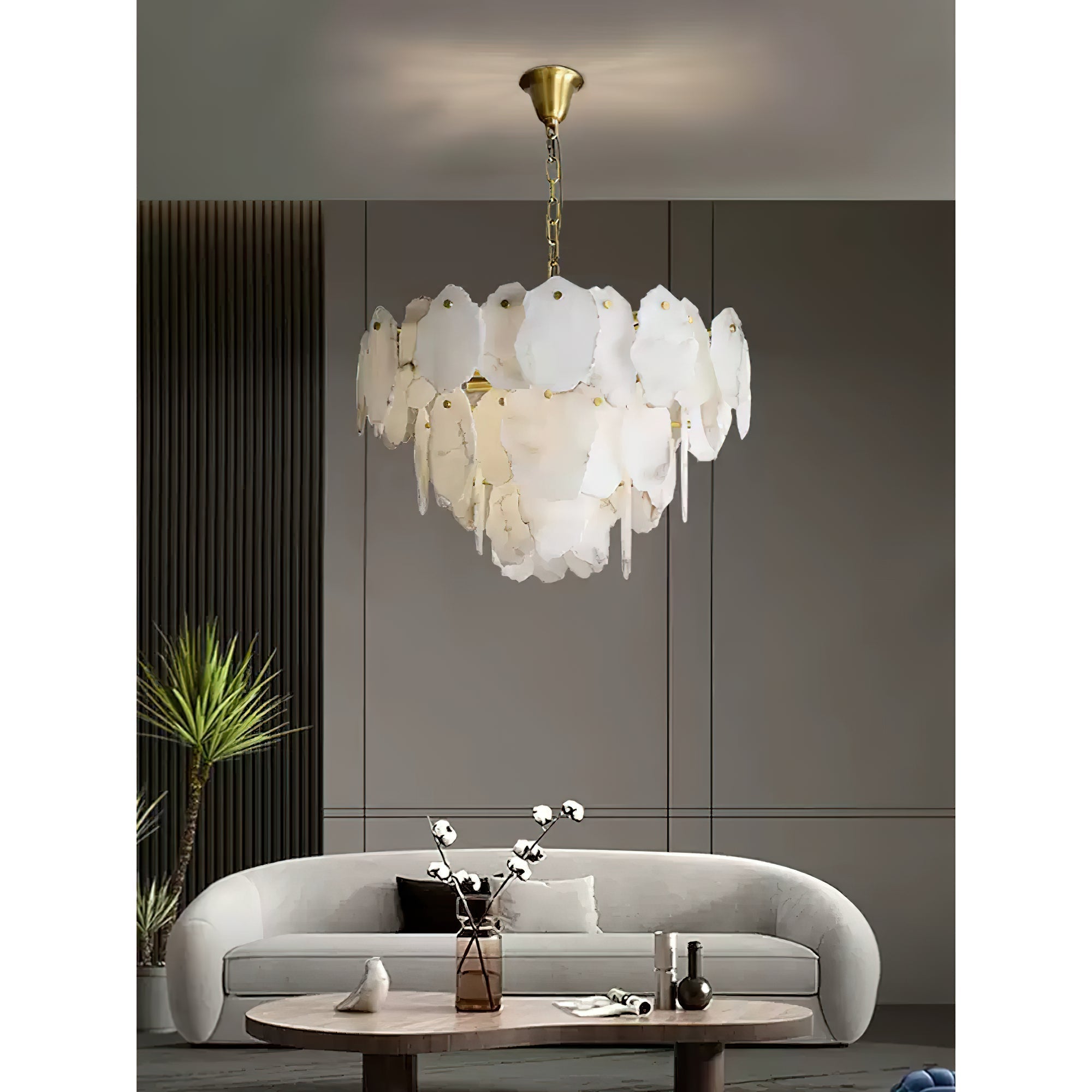 Clérachic Gloire alabaster chandelier over a curved cream sofa, its stone tiers glowing warm against a taupe panelled wall.