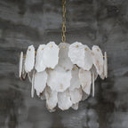 Unlit view of the Clérachic Gloire alabaster chandelier against grey limewash, showing every raw-cut edge and brass fixing pin.