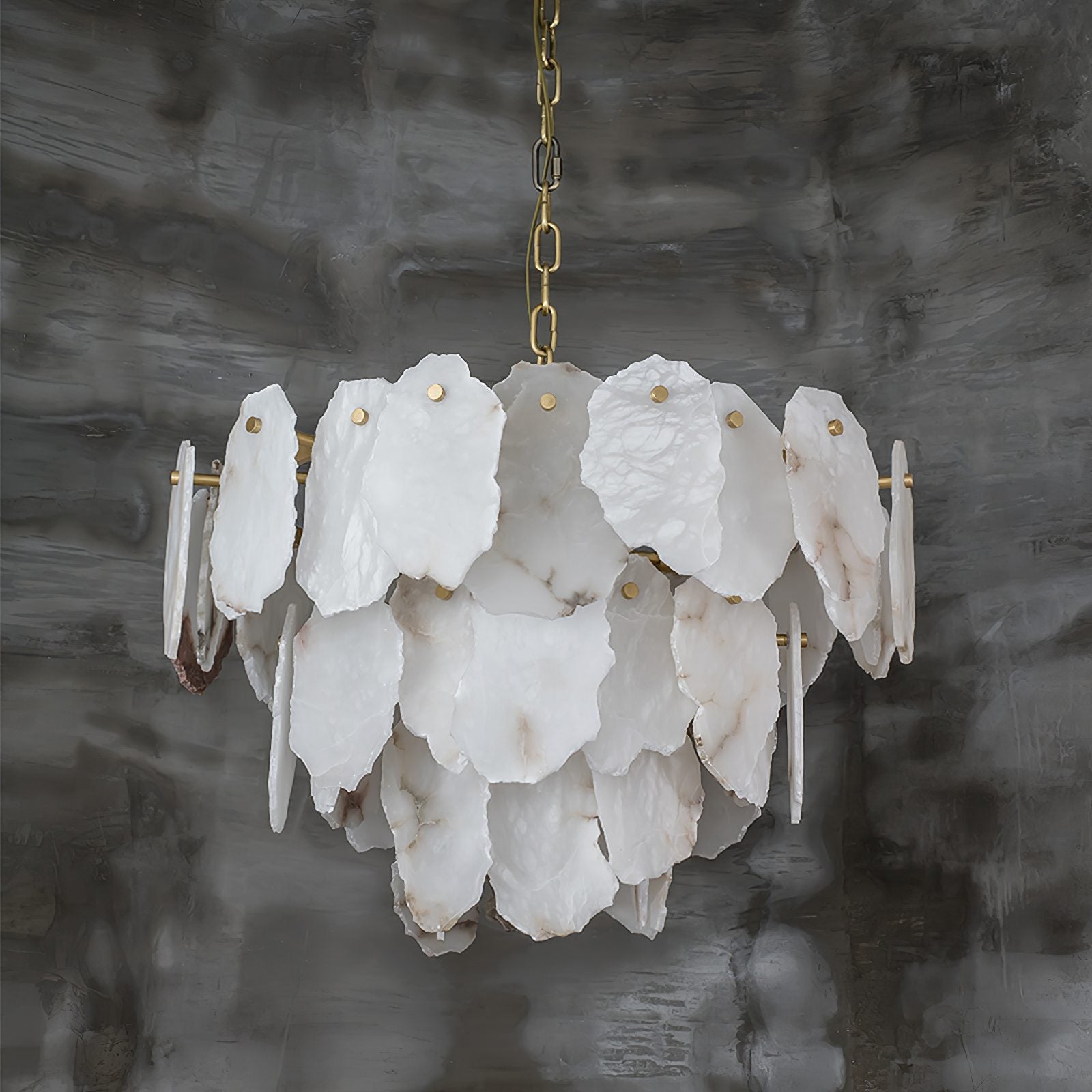 Unlit view of the Clérachic Gloire alabaster chandelier against grey limewash, showing every raw-cut edge and brass fixing pin.