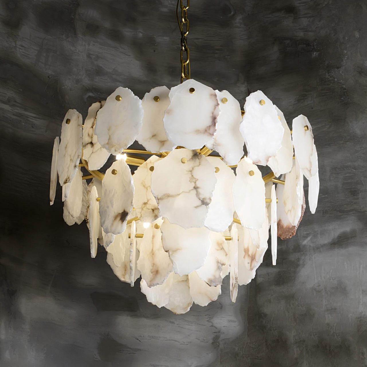 Close view of the lit Clérachic Gloire chandelier, brass arms visible behind three staggered rings of alabaster.