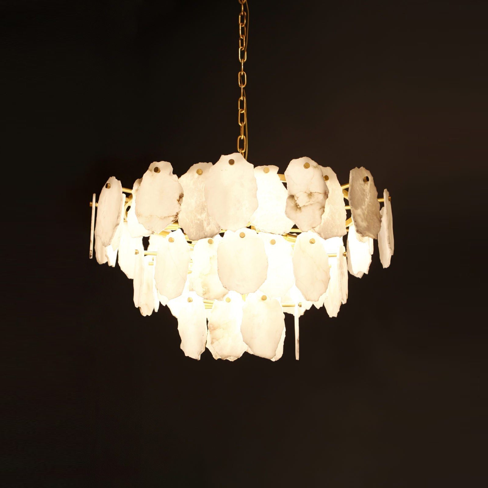 Clérachic Gloire alabaster chandelier fully lit against black, each stone plate glowing from within on its brass chain.