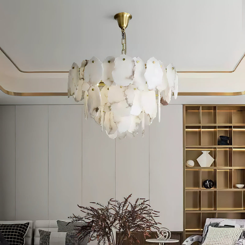 Clérachic Gloire alabaster chandelier lit above a living room with brass shelving and a stepped, gold-trimmed ceiling.