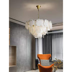 Clérachic Gloire chandelier against a concrete-panelled wall, glowing beside an orange velvet armchair and sheer curtains.
