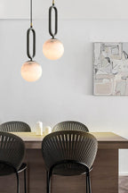 The Clérachic Gloruvyd pair hung at staggered drops above a dining table, alabaster globes glowing over black fan-back chairs.