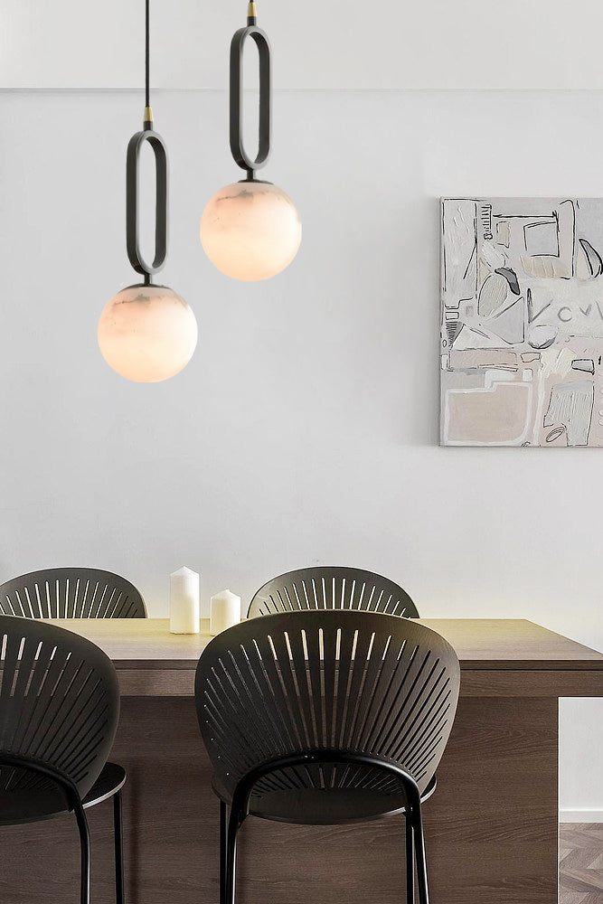 The Clérachic Gloruvyd pair hung at staggered drops above a dining table, alabaster globes glowing over black fan-back chairs.