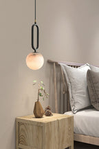 The Clérachic Gloruvyd pendant hangs low over an oak nightstand, its black frame crisp against a warm grey bedroom wall.