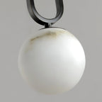 Clérachic Gloruvyd in close-up, the black frame's arc meeting a hand-carved alabaster globe streaked with grey veining.