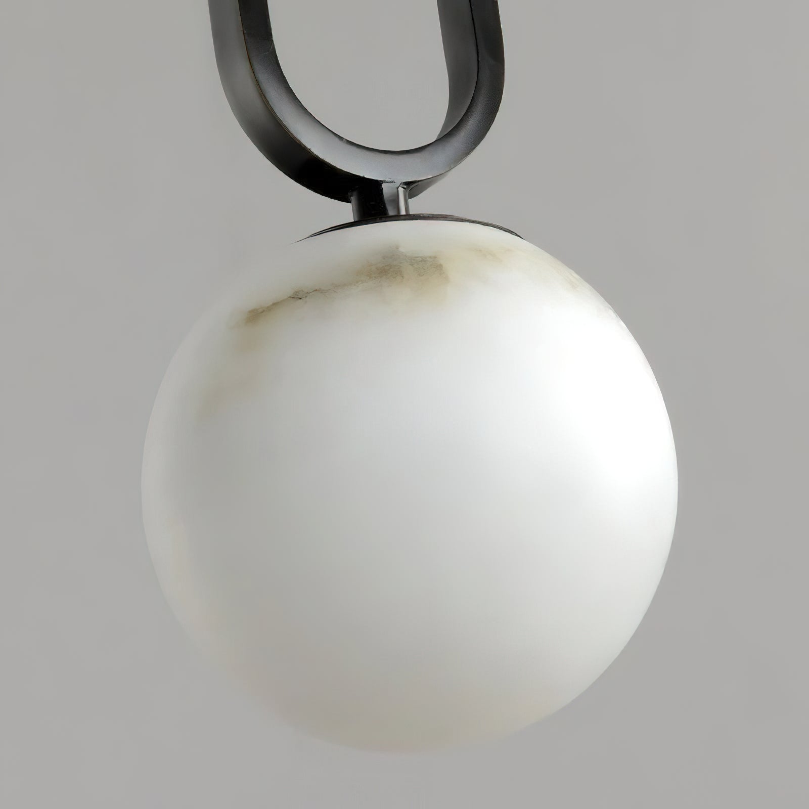 Clérachic Gloruvyd in close-up, the black frame's arc meeting a hand-carved alabaster globe streaked with grey veining.