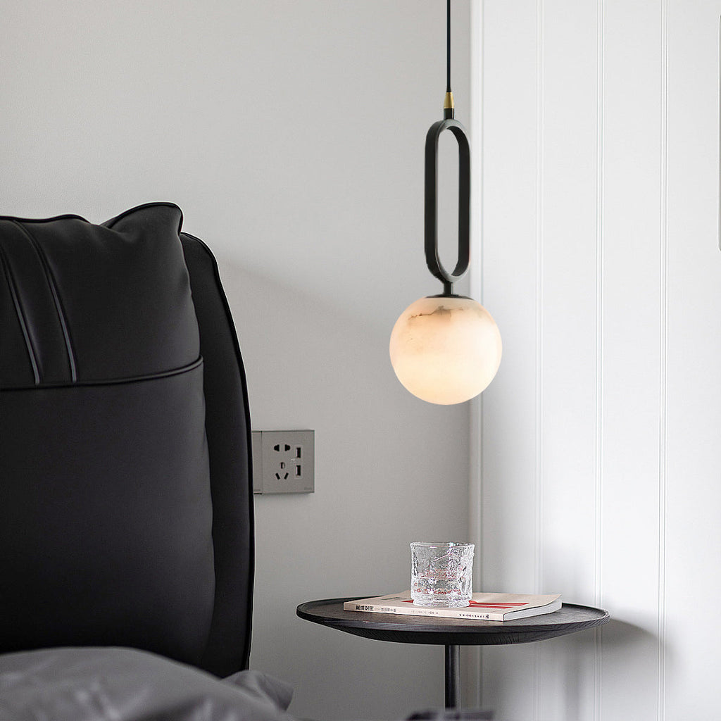 The Clérachic Gloruvyd pendant beside a black leather headboard, alabaster globe lit above a round bedside table.