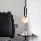 The Clérachic Gloruvyd pendant beside a black leather headboard, alabaster globe lit above a round bedside table.