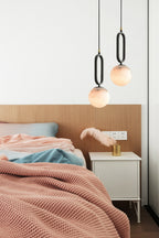 The Clérachic Gloruvyd pendants flank an oak headboard at uneven drops, warm stone light over pink and blue bedding.