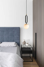 Clérachic Gloruvyd hangs beside a blue upholstered headboard, its alabaster ball above a black glass-top nightstand.