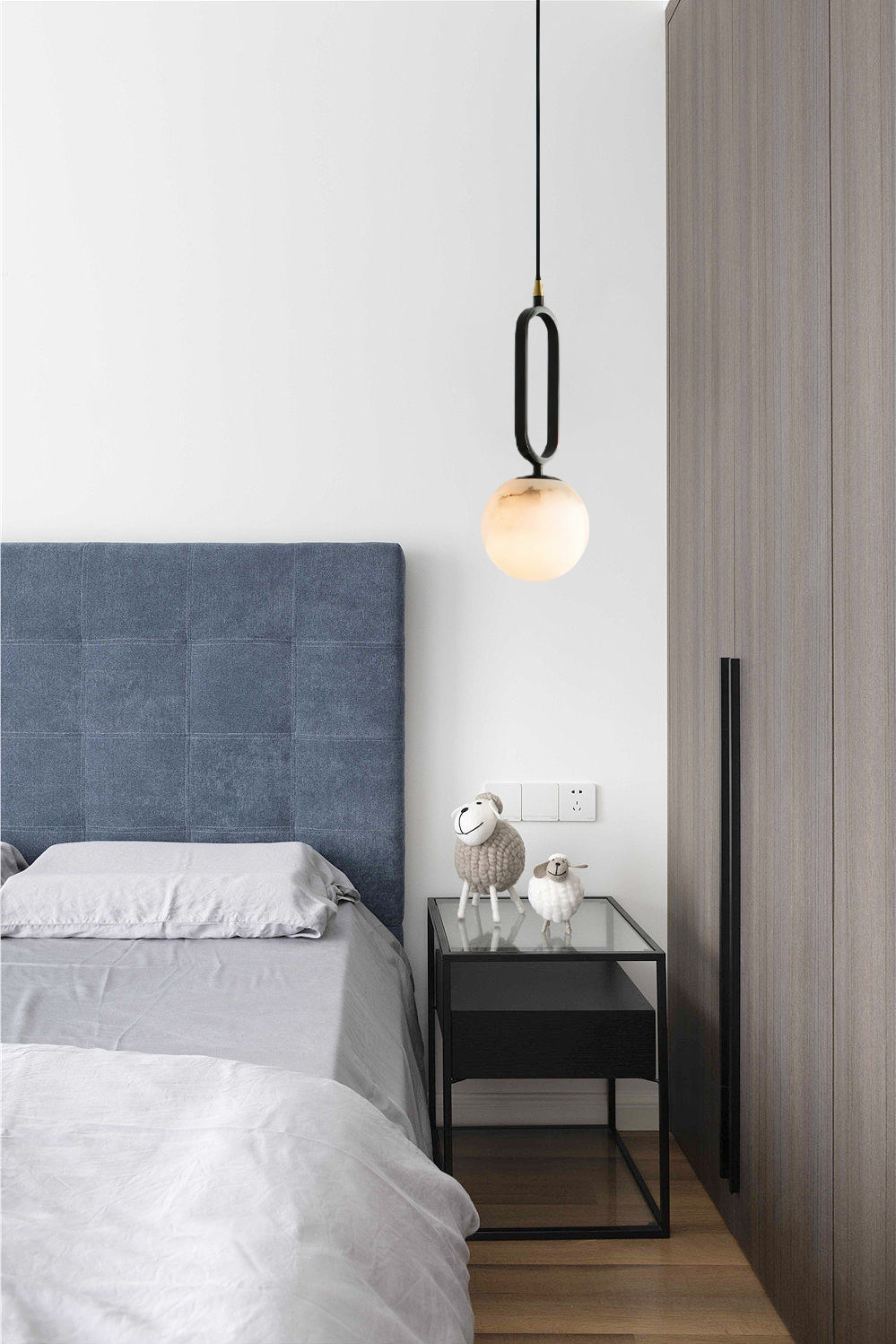 Clérachic Gloruvyd hangs beside a blue upholstered headboard, its alabaster ball above a black glass-top nightstand.