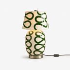 Glossy cream ceramic body and tapered shade painted with looping dark-green strokes, on a brushed metal base with an in-line switch, shown on white for this Clérachic table lamp.