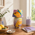On a wooden desk with a lemon bowl, a lilac pen pot and notebooks, this Clérachic table lamp shows its colourful painted shade and body.