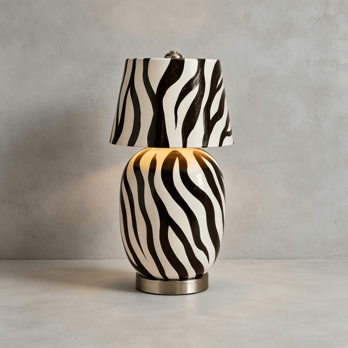 The striped version of this Clérachic table lamp stands on a pale concrete surface, its body glowing faintly through the black-and-white pattern.