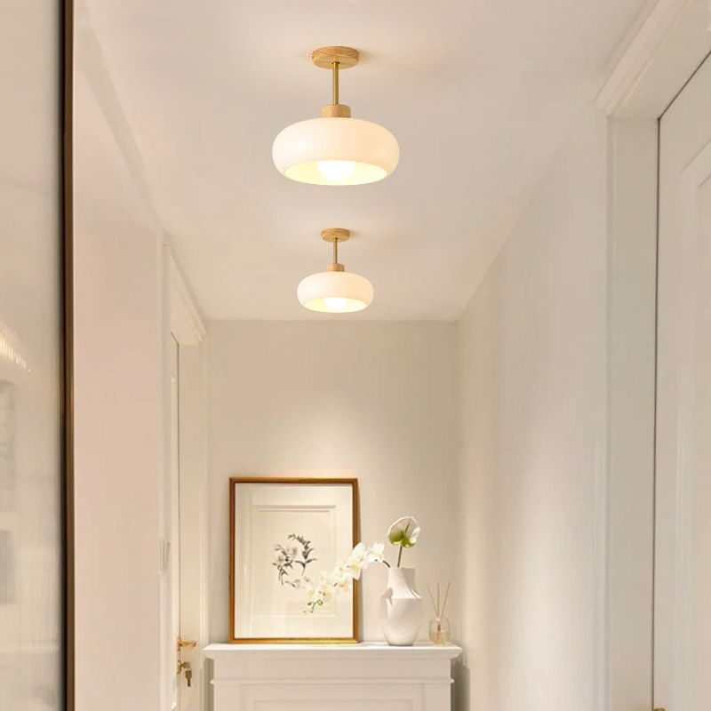 Two Clérachic glossy dome semi-flush ceiling lights in white, lit down a bright hallway above a framed print and vase.
