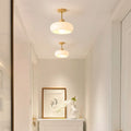 Two Clérachic glossy dome semi-flush ceiling lights in white, lit down a bright hallway above a framed print and vase.