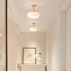 Two Clérachic glossy dome semi-flush ceiling lights in white, lit down a bright hallway above a framed print and vase.