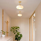 A pair of Clérachic white dome ceiling lights in a wood-trimmed corridor above a coat stand and leafy plant.