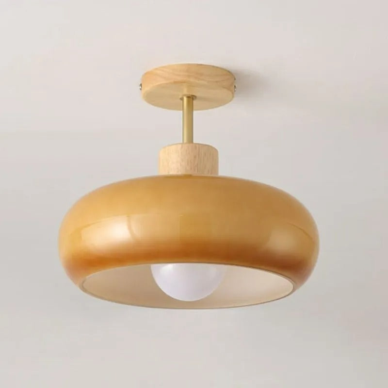 Clérachic dome ceiling light in orange, its round wood canopy and exposed bulb seen against a warm plain wall.