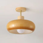 Clérachic dome ceiling light in orange, its round wood canopy and exposed bulb seen against a warm plain wall.