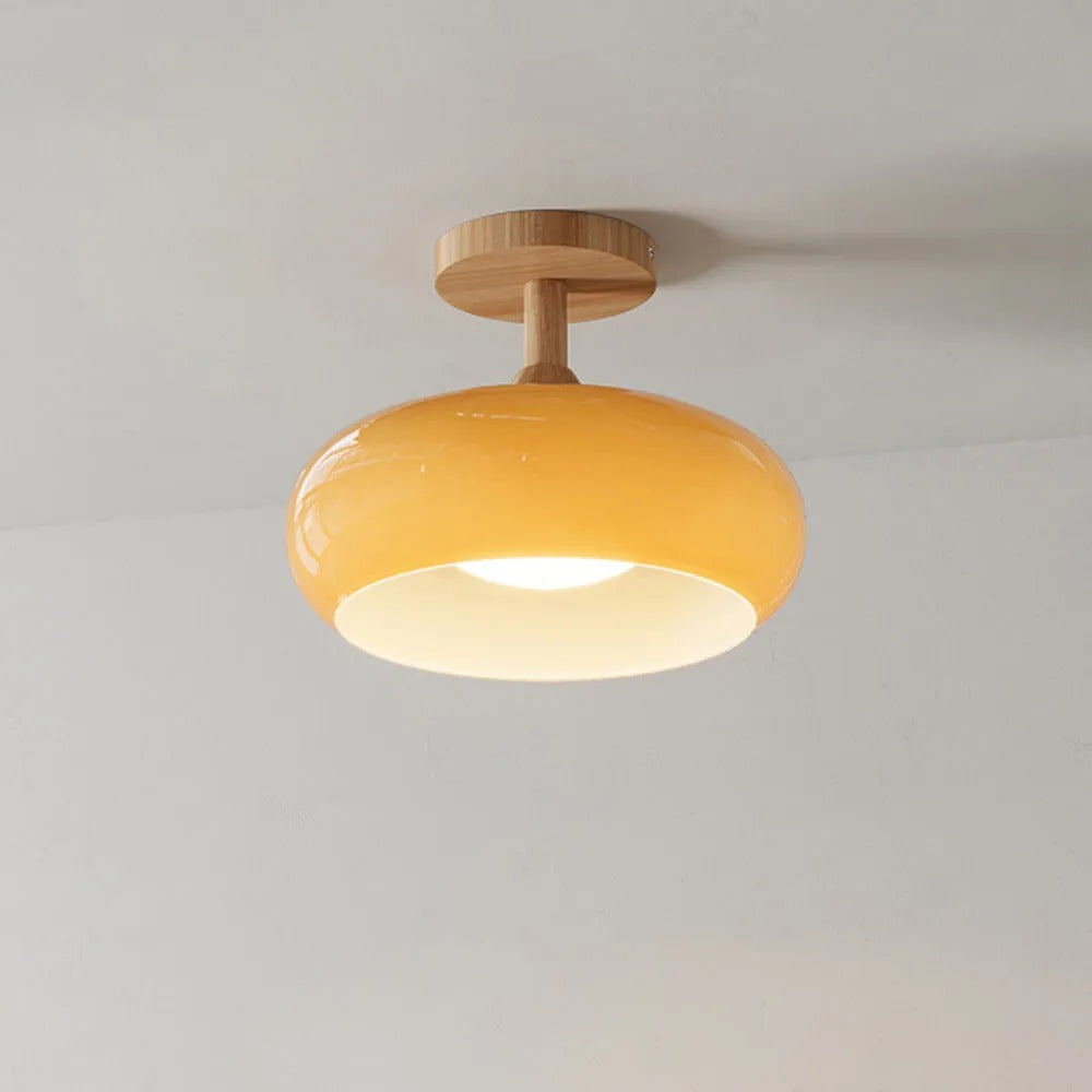 Clérachic dome ceiling light in glossy yellow-orange, lit against a plain wall with the white inner disc glowing.