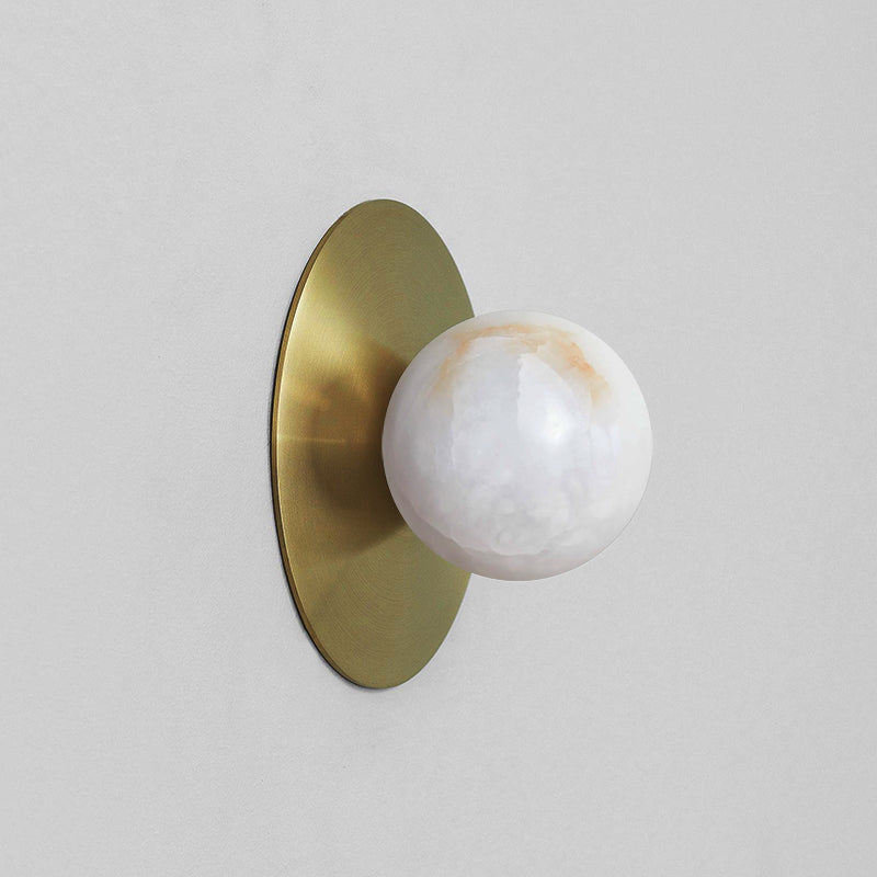Clérachic Glow wall sconce in brass on a pale wall, warm veining running through the globe.
