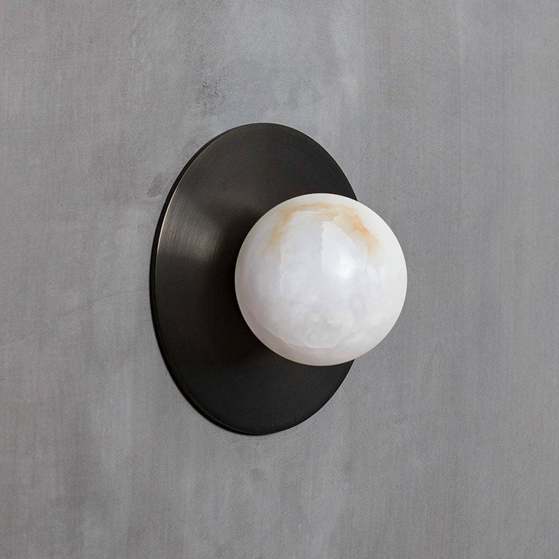 Clérachic Glow sconce in black on grey concrete, the alabaster globe catching soft daylight.